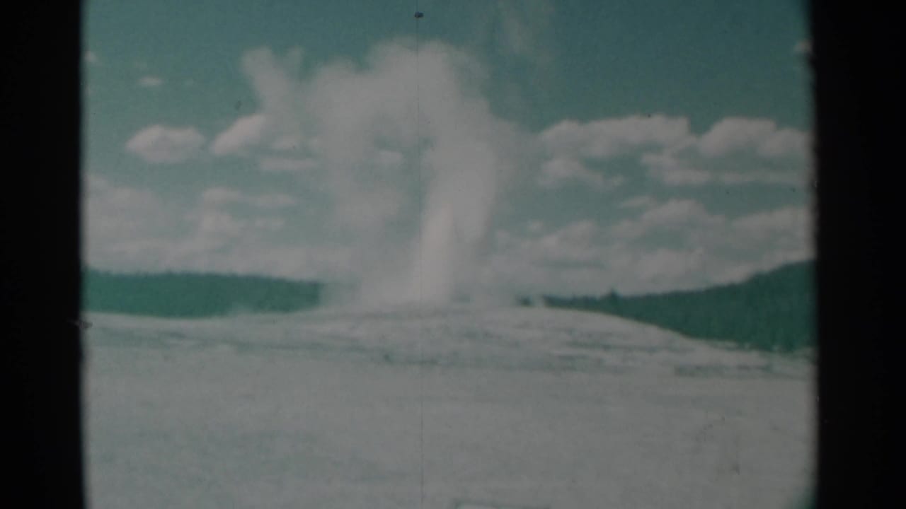 White smoke plume rising over flat open ground beneath a cloudy sky.