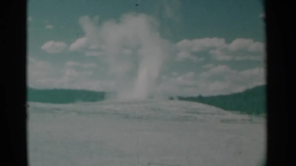 1961 8mm frame from Cheyenne, Wyoming showing a distant white smoke plume rising over open terrain under scattered clouds.