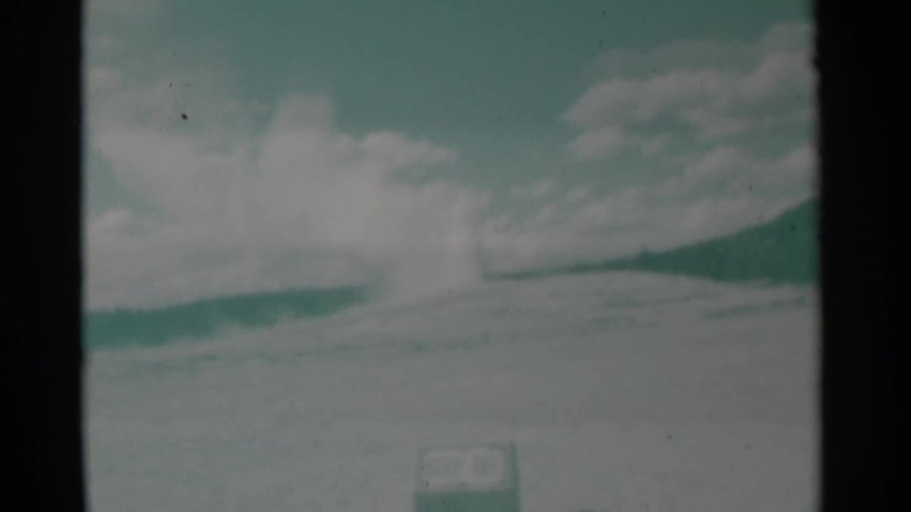 Steam rises at the crest of a low hill under a cloudy sky, with a small sign low in frame.