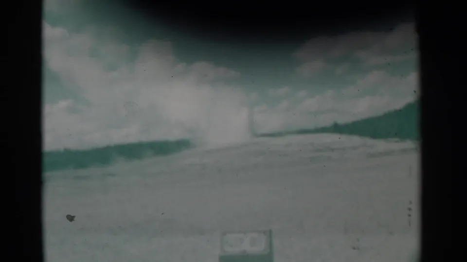 Aged 8mm frame from the Wyoming clip showing steam rising beyond pale ground, with clouds overhead and a dark contact-sheet bar crossing the view.