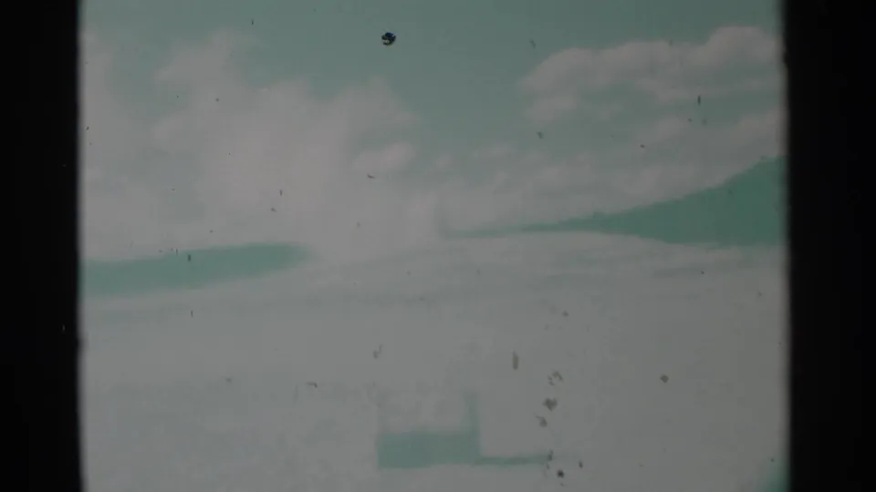 1961 Wyoming 8mm frame showing a pale landscape, distant steam plume, soft clouds, and faint foreground sign in muted aged-film color.