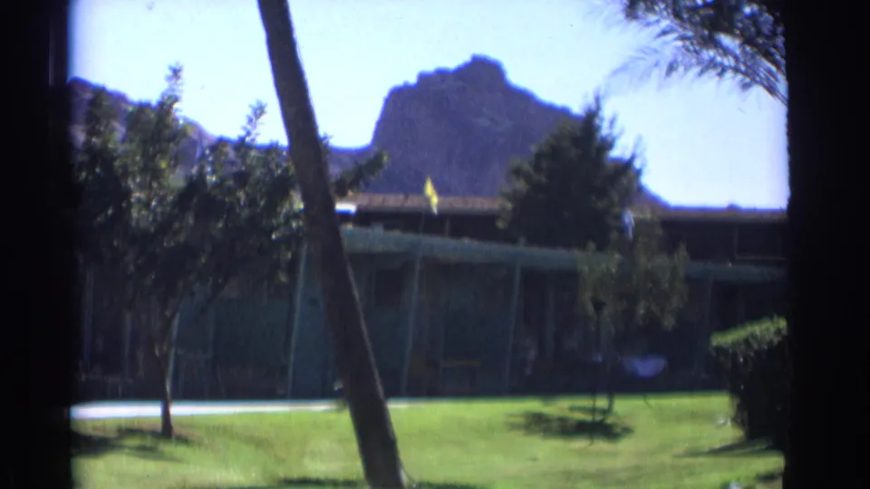 Cataloged 1961 Cheyenne, Wyoming 8mm frame showing a resort-like exterior, lawn, palm trees, shrubs, and rocky mountain backdrop.