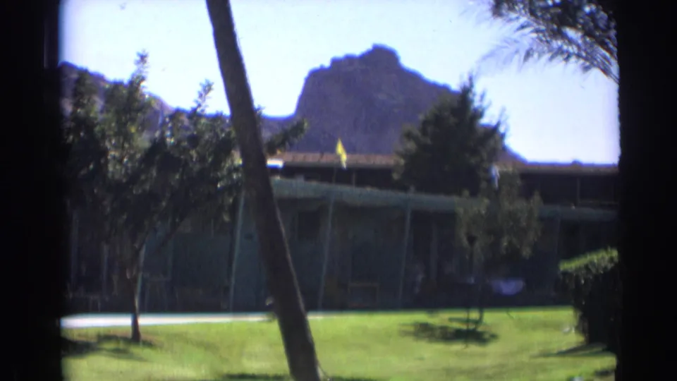 Cataloged 1961 Cheyenne, Wyoming 8mm frame with a palm trunk foregrounding a resort-like building and mountain view.