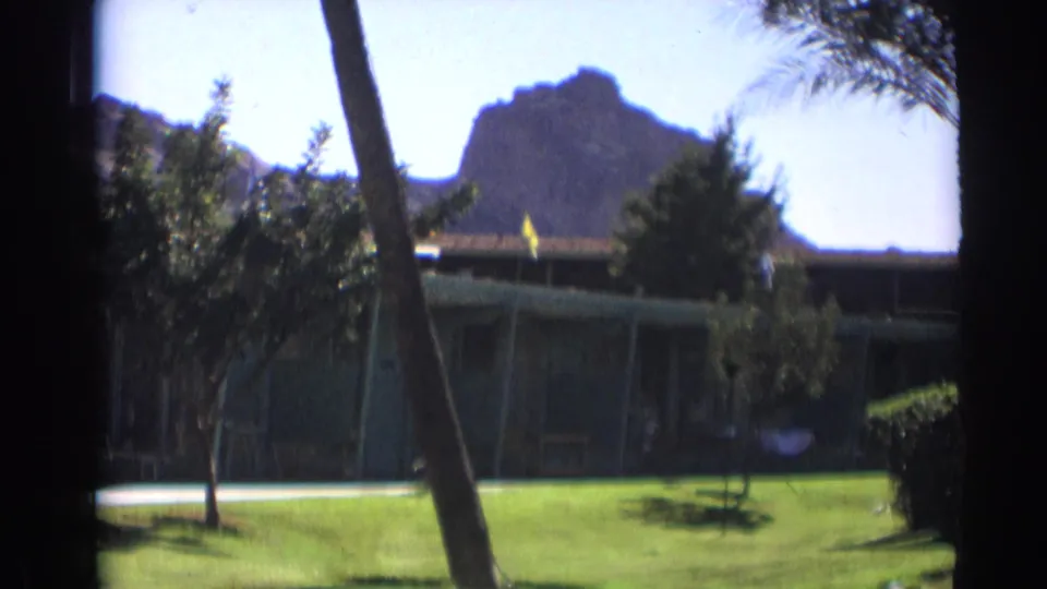 1961 home-movie frame from the stated Cheyenne, Wyoming clip showing a low motel building, green lawn, palms, and a mountain backdrop.