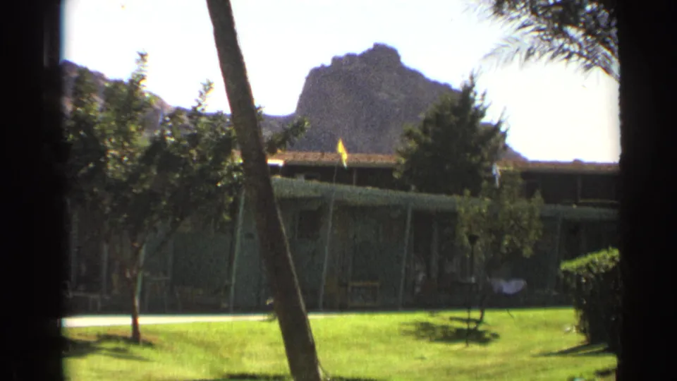 Cheyenne, Wyoming 1961 home-movie still showing lawn, trees, a low building, and a rocky butte through soft 8mm color.