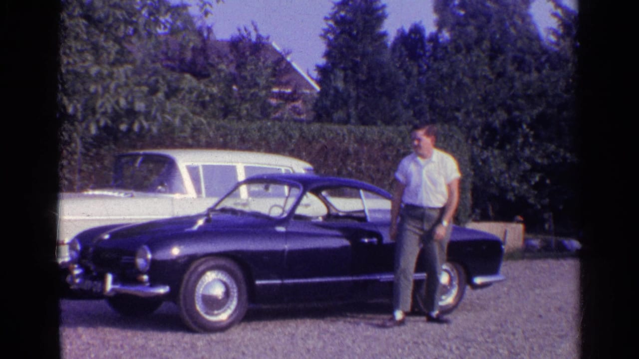 Man standing beside a blue classic coupe in a driveway.