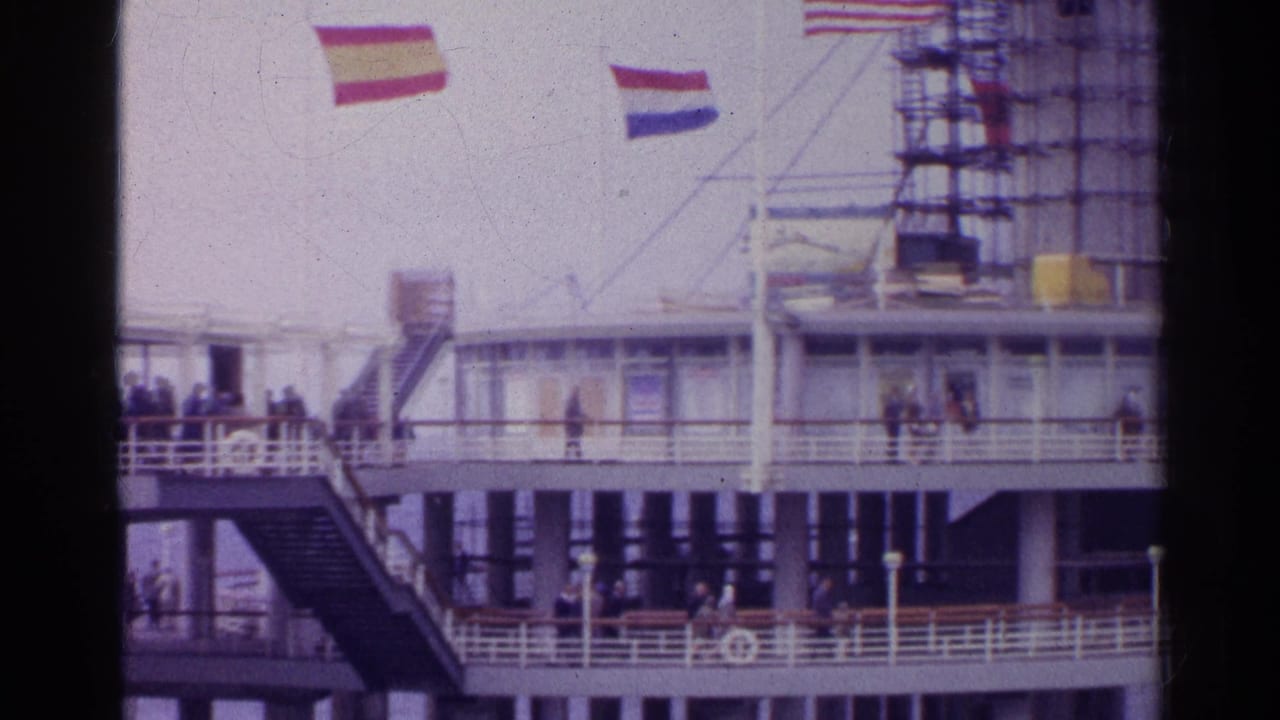 1961 8mm view of a ship deck with passengers, railings, and American, Dutch, and other flags visible overhead.
