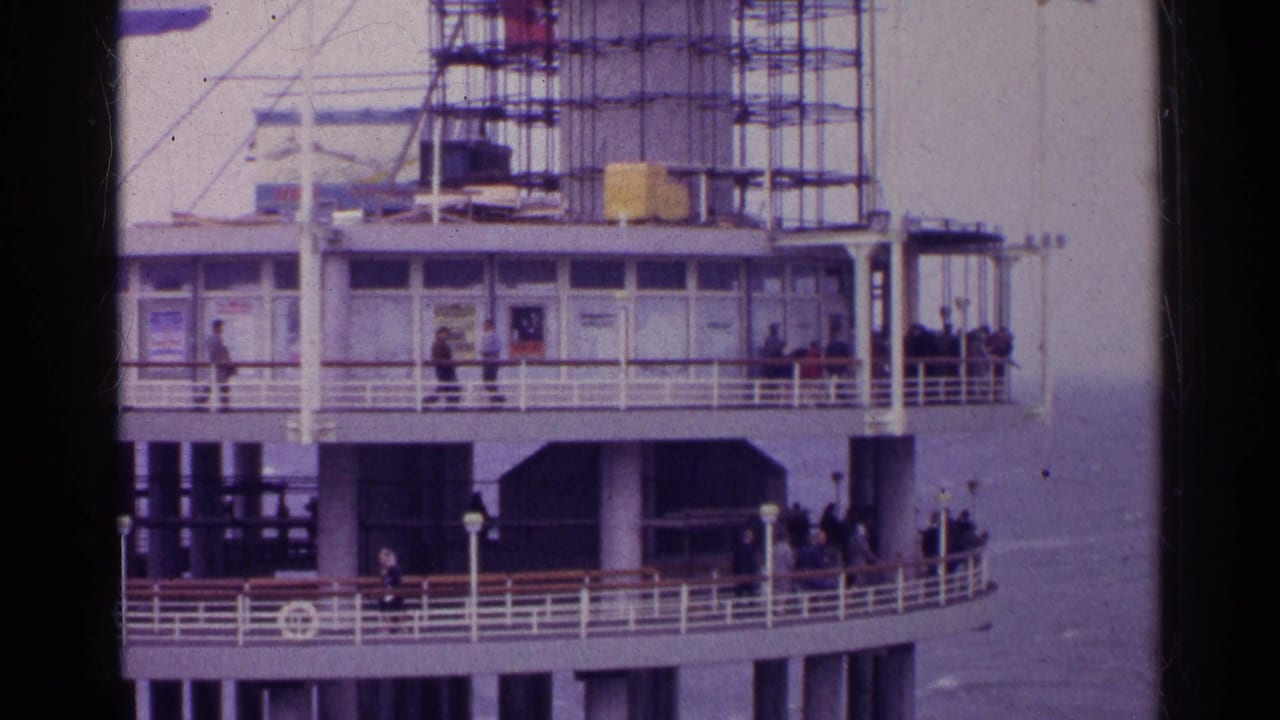Multi-level waterfront pier with people on railings and scaffolding above.