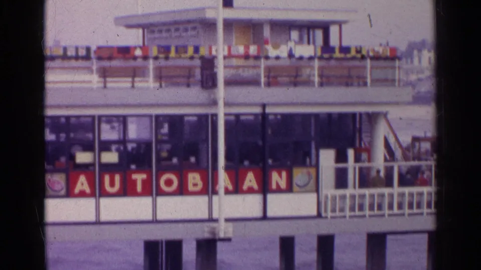 1961 Germany waterfront pier with AUTOBAAN signage, flags along the upper deck, and visitors near the railings.