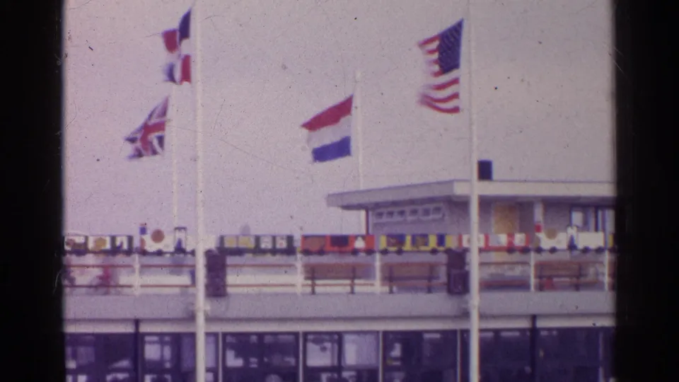 1961 Germany home-movie view focused on national flags, upper railings, and the roofline of a ferry or transport terminal.