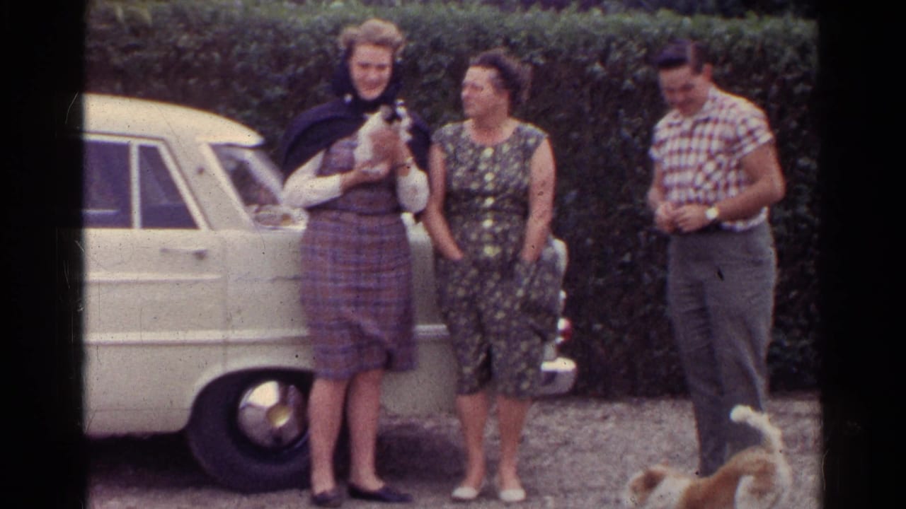 Three adults in period clothing stand near a light-colored classic car and small dogs in the supplied Germany home-movie footage.