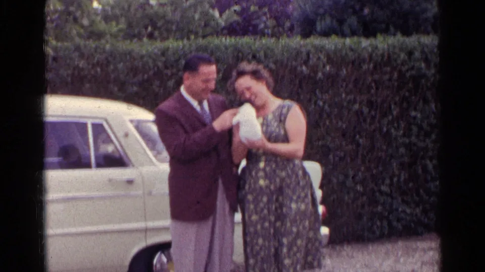 The final frame shows the woman smiling down at the puppy as the suited man stands beside her in the 1961 German garden scene.