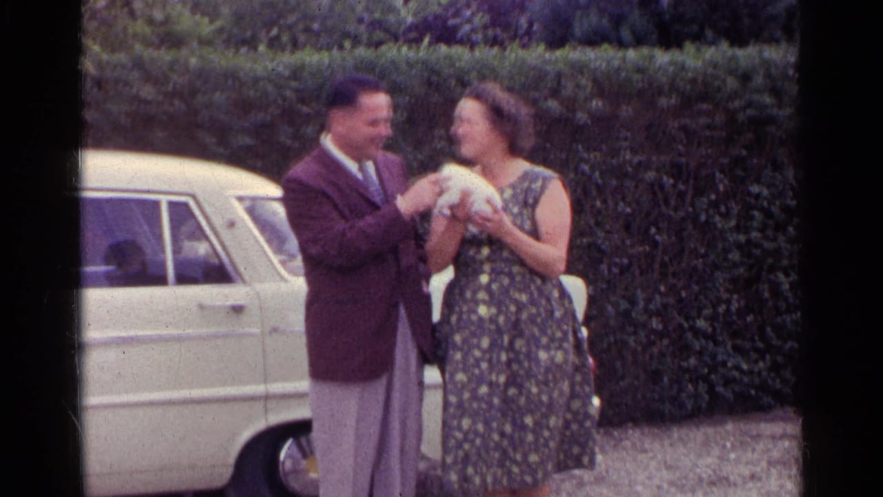 Couple standing beside a light-colored car while holding a small puppy.