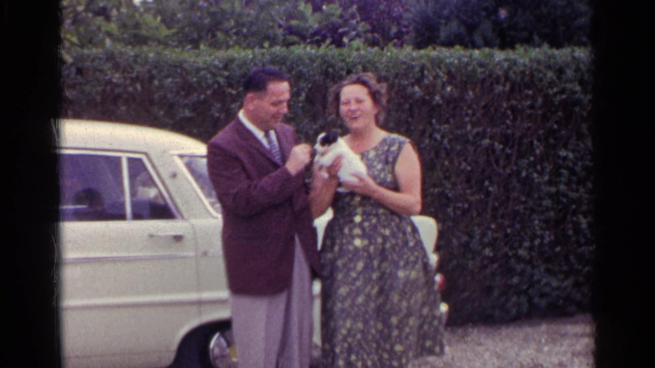 Man and woman smiling with a puppy in front of a hedge and car.