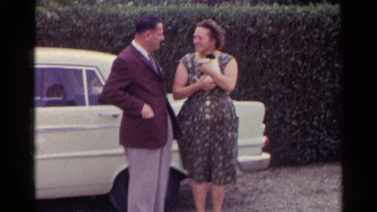 Couple smiles near a white car while the woman holds a small kitten.
