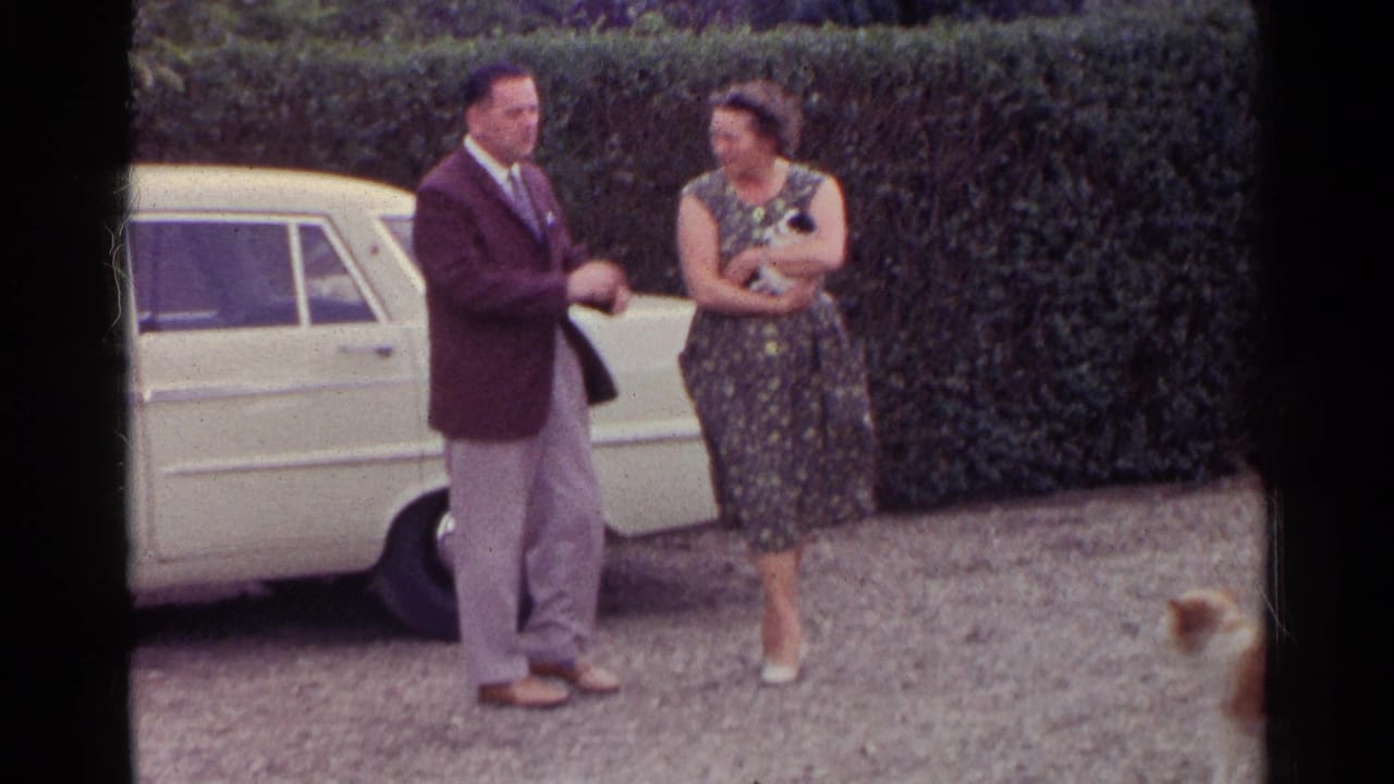 Man gestures while woman stands smiling near the rear of a cream car.