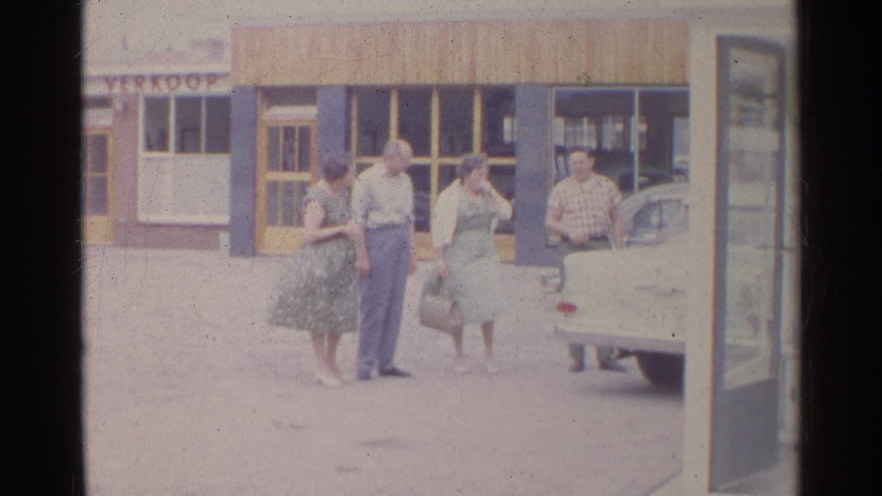 Two couples in mid-century clothing stand beside a parked car outside a storefront in footage identified as Germany, 1961.