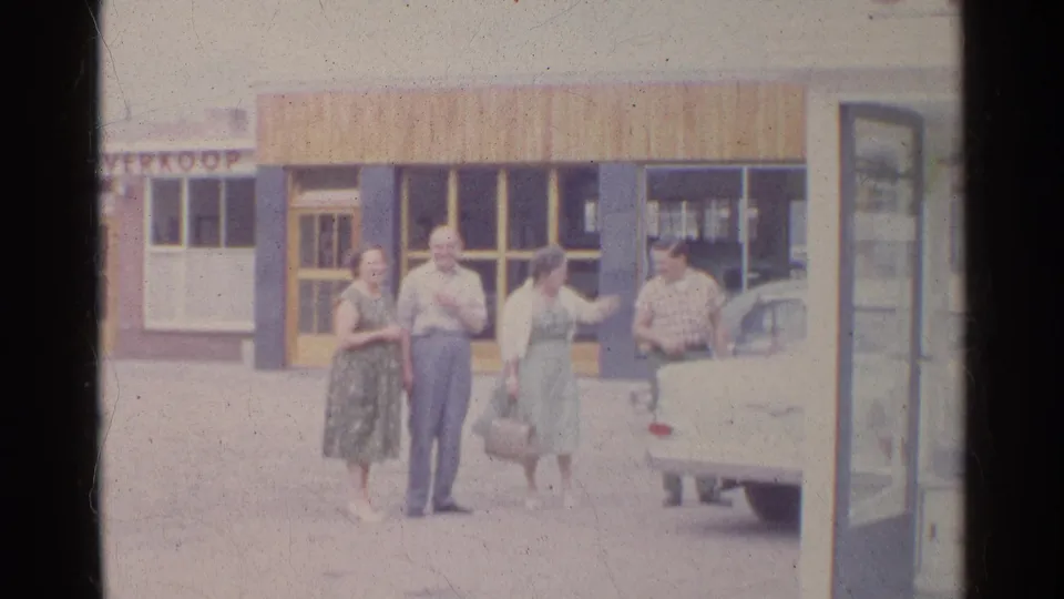 A woman gestures toward a man beside the car while the other adults look on in this 1961 Germany street scene.