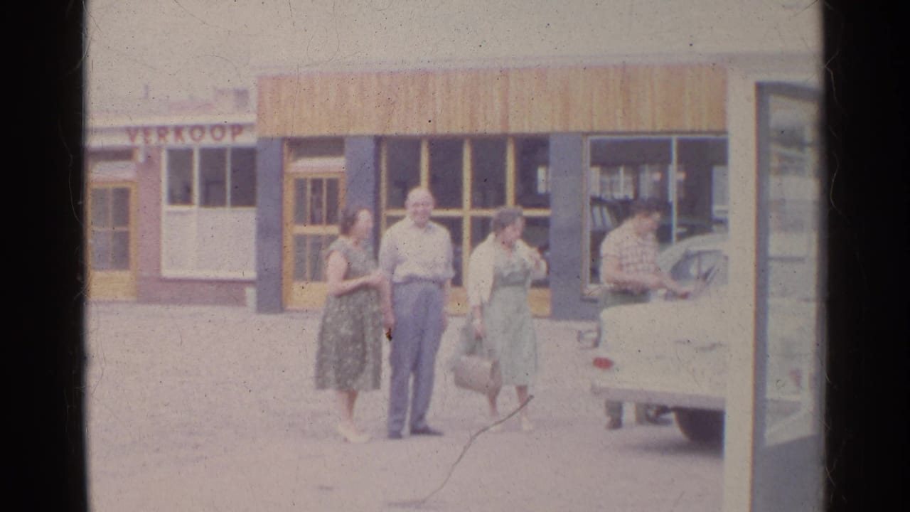 Adults standing outside a storefront beside a white vintage car.