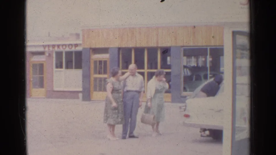 Adults outside a German storefront in 1961, with a woman holding a handbag and another man bent into a white car.