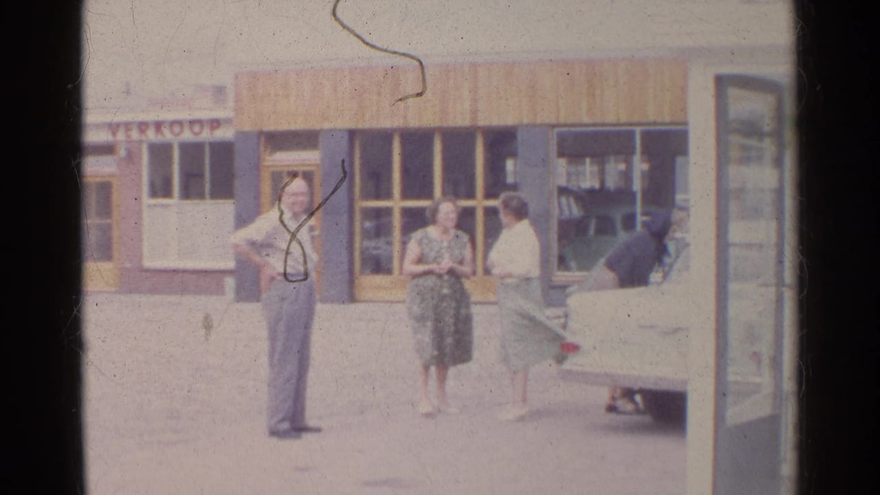 1961 Germany frame showing adults in period clothing near a storefront and parked white car.