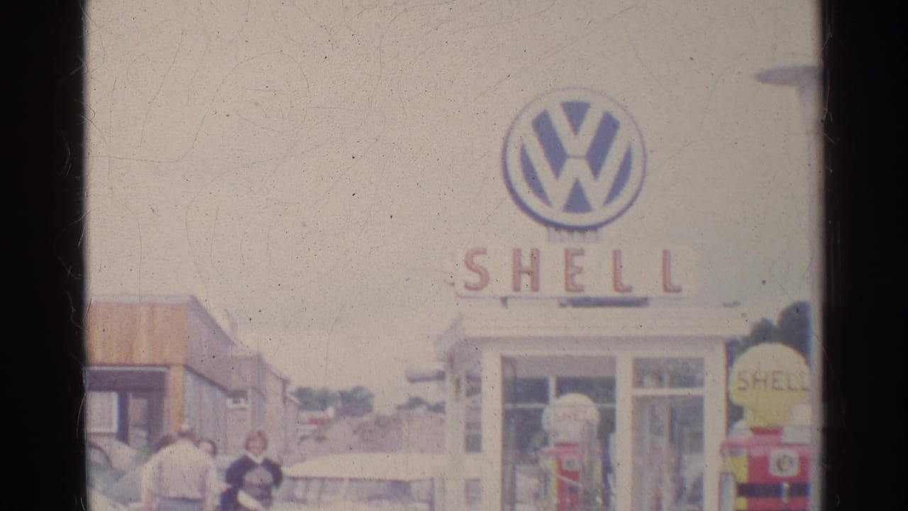 1961 Germany frame of a Shell station with Volkswagen branding, retro pumps, a light-colored car, and adults standing nearby.