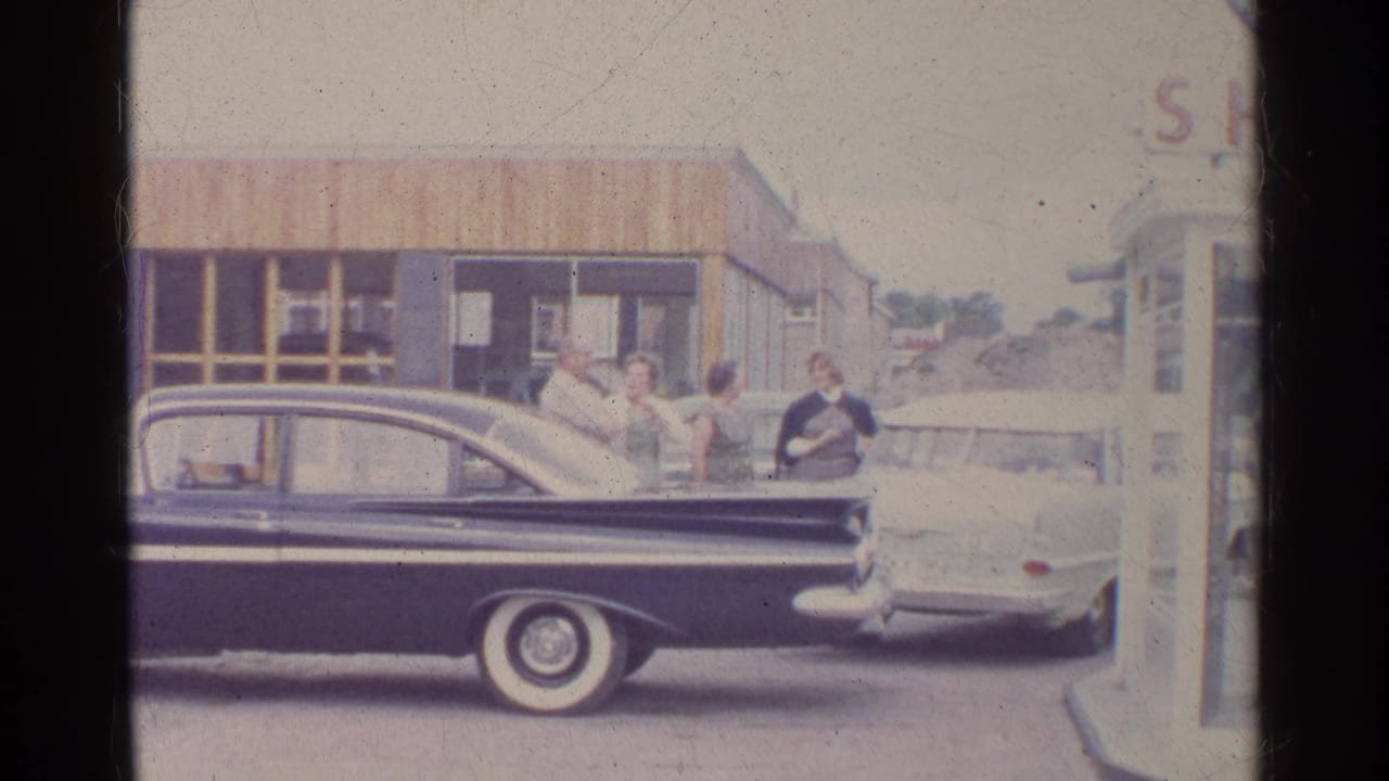 People stand beside two cars near the pump area of a Shell station.