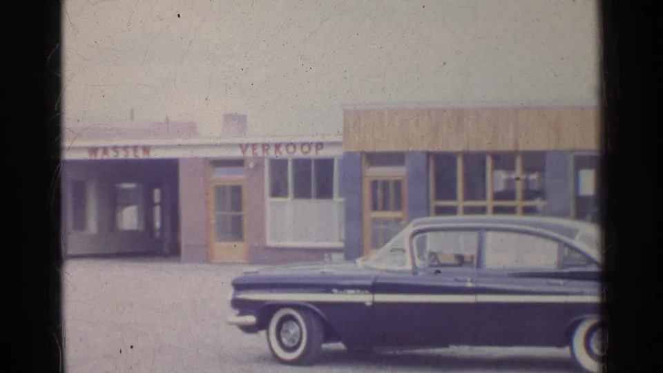 1961 Germany-labeled 8mm frame with a cropped dark sedan in the foreground of storefronts marked WASSEN and VERKOOP.