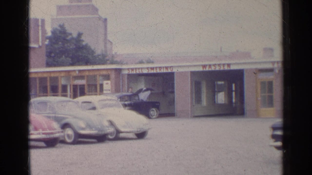 1961 Germany home-movie view of classic cars lined up before a low service-station building with wash signage and storefront windows.