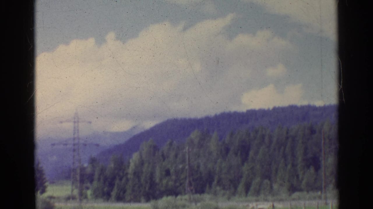 A brief Germany 1961 landscape view shows a wooded hillside beneath large clouds, with fields and a distant utility pylon.