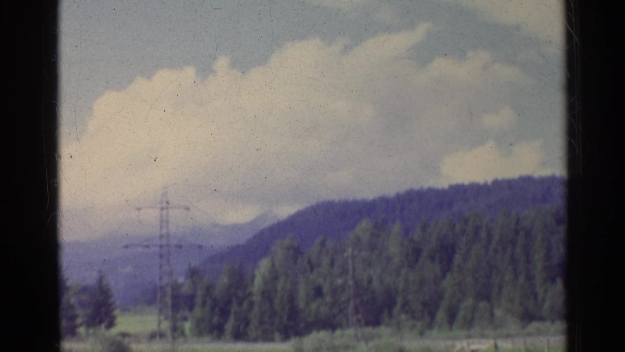 Green countryside with wooded hills, clouds, and an electricity pylon seen through dark frame edges.