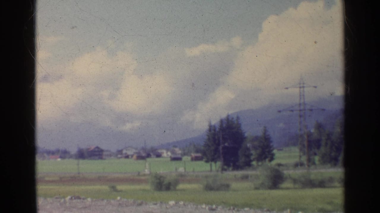 Rural Germany in 1961 appears in soft 8mm color, with fields, a village edge, trees, pylons, and mountains in the distance.
