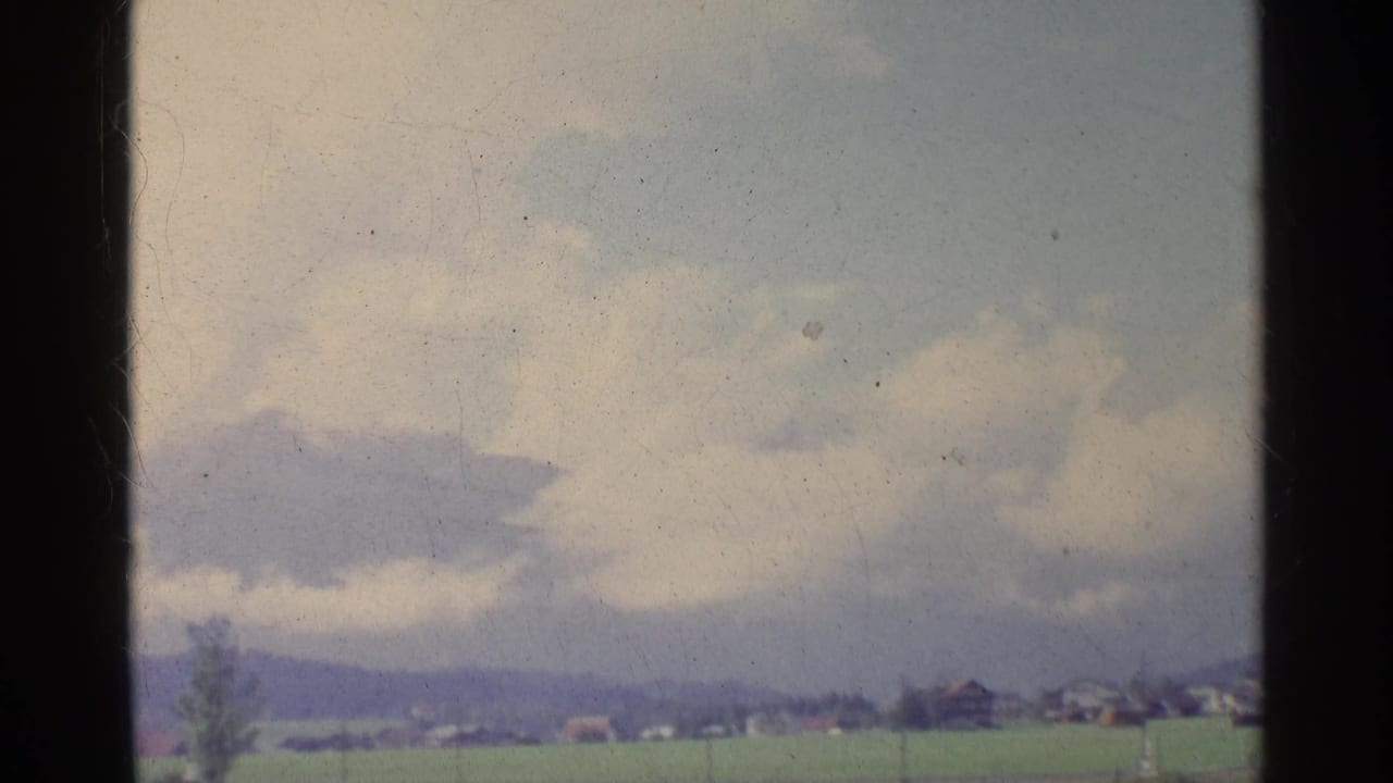 1961 German countryside view through a window frame, with green fields, distant hills, village roofs, and a cloudy sky.