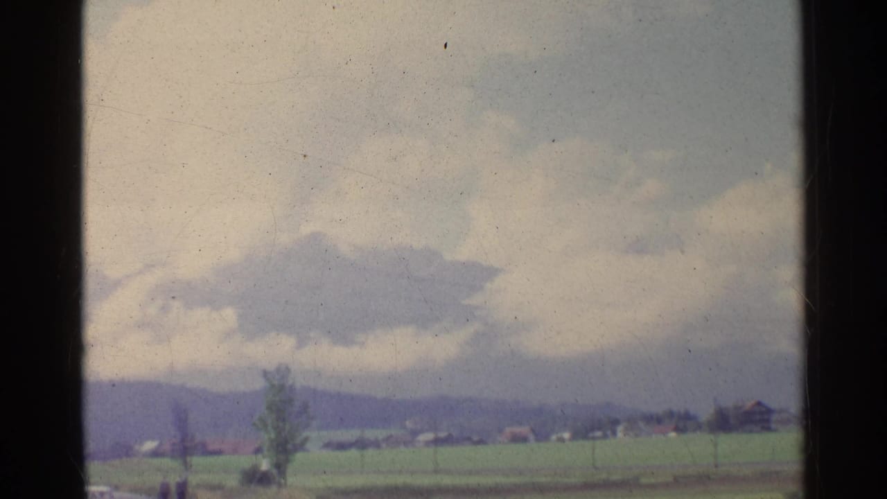 Green rural fields and low hills under clouds, divided by a dark window post.