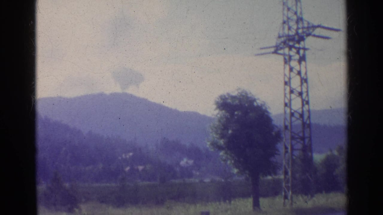 Faded 1961 Germany countryside frame showing wooded mountains, open fields, a lone tree, and an electricity pylon near the foreground.