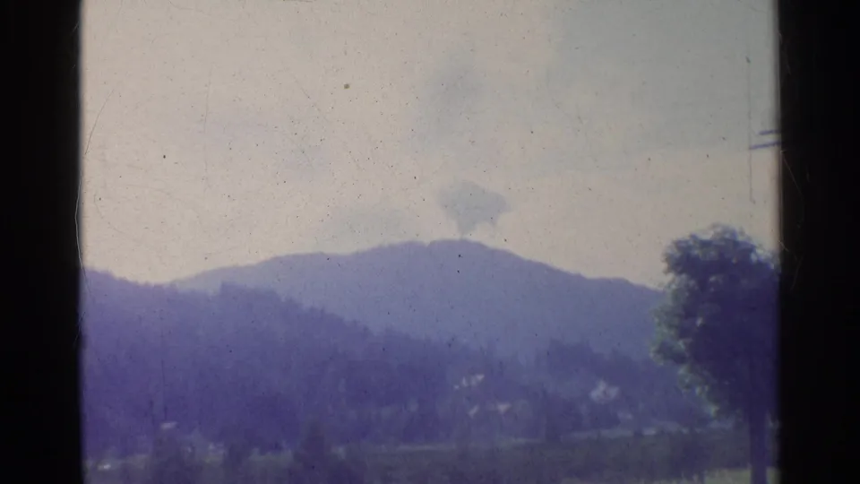 1961 German 8mm home-movie view of wooded hills and distant buildings framed by dark window mullions.