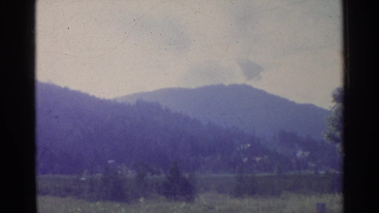 1961 German countryside scene with soft wooded hills, a meadow, and distant structures behind dark window framing.