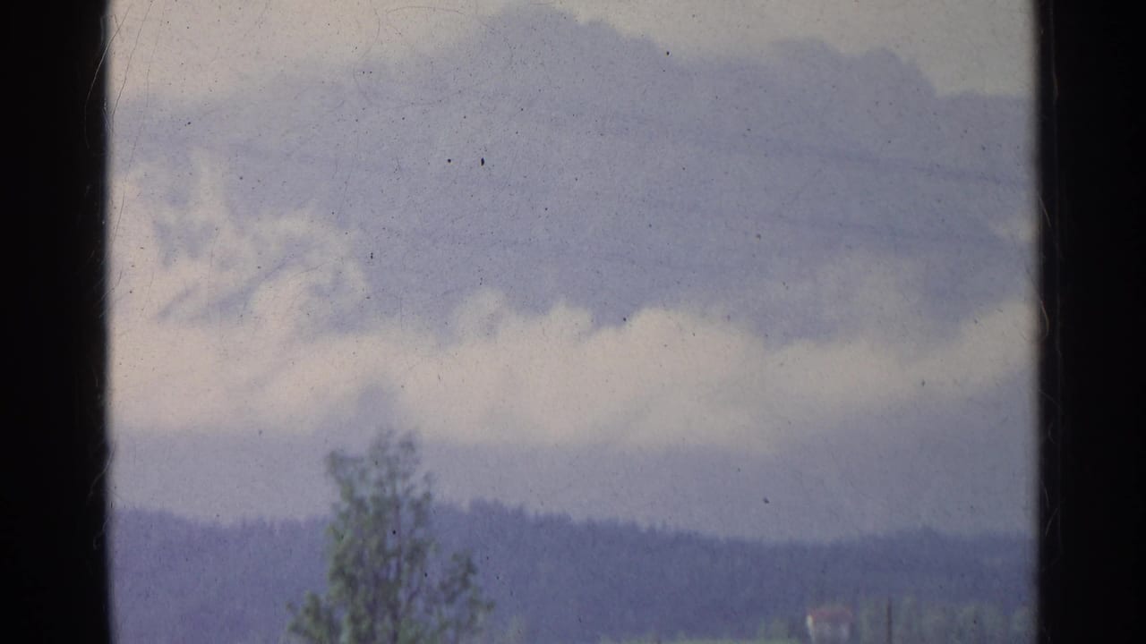 1961 Germany 8mm frame showing power lines crossing a cloudy sky above distant hills, with dark window-like edges.