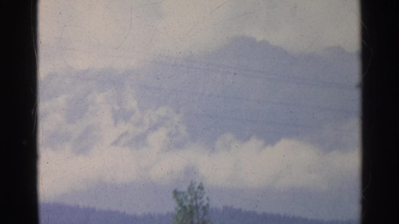 Faded 8mm view from Germany in 1961, showing power lines across a cloudy sky over a distant hillside and tree top.