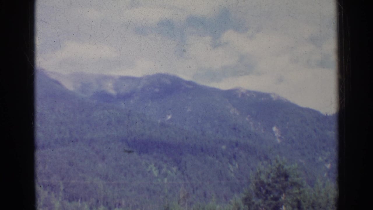 1961 German 8mm frame showing a cloudy mountain ridge above evergreen forest, seen through dark window-like framing.