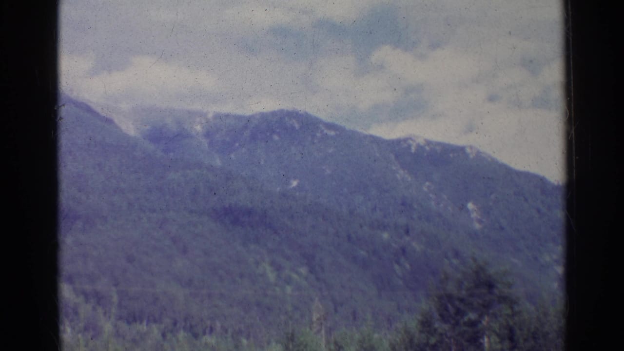 Soft 8mm frame from Germany in 1961 showing a muted mountain ridge, forest canopy, and overcast sky.