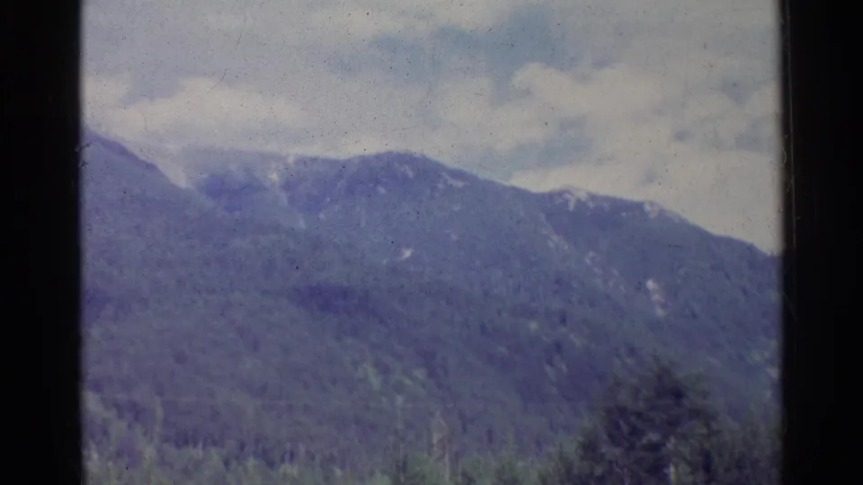 Soft 8mm frame from Germany in 1961 showing a muted mountain ridge, forest canopy, and overcast sky.