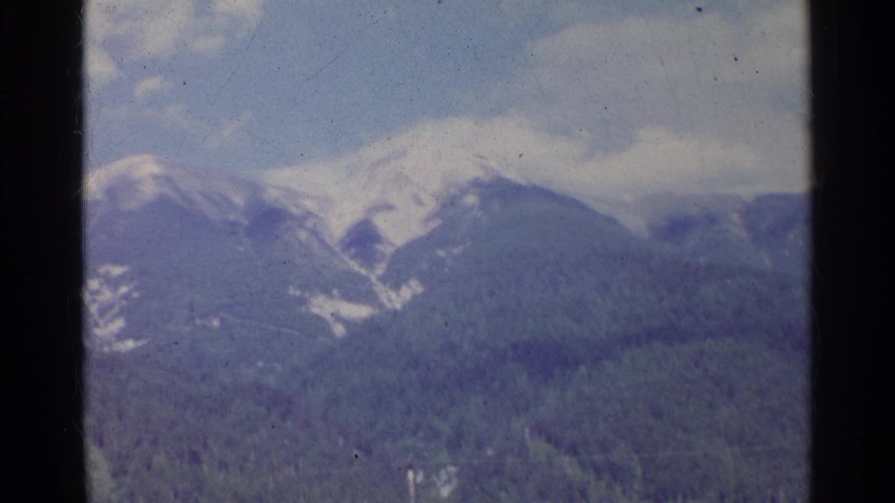 1961 Germany 8mm frame showing a distant snow-capped mountain over evergreen forest with visible film wear.