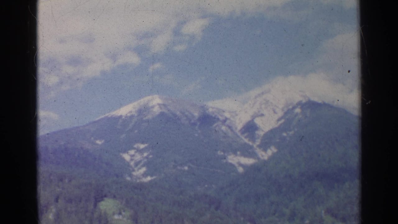1961 Germany 8mm frame showing snow-covered peaks behind forested foothills, with soft color and visible film wear.