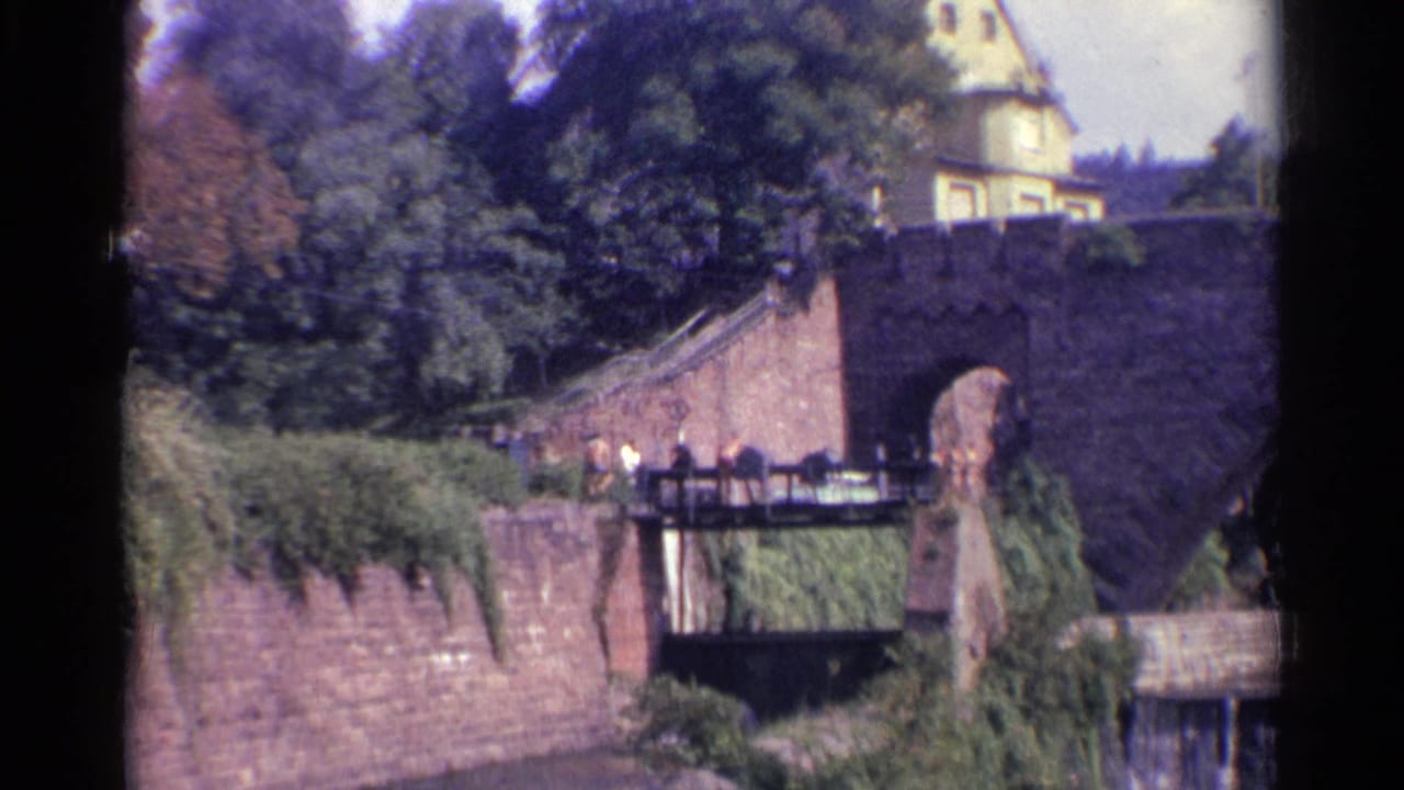 Final 1961 Germany frame showing the stone arch bridge, lower pedestrian crossing, dense foliage, and a partly visible yellow building.