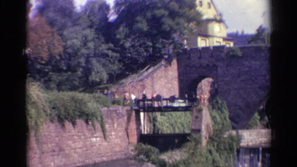 Final 1961 Germany frame showing the stone arch bridge, lower pedestrian crossing, dense foliage, and a partly visible yellow building.
