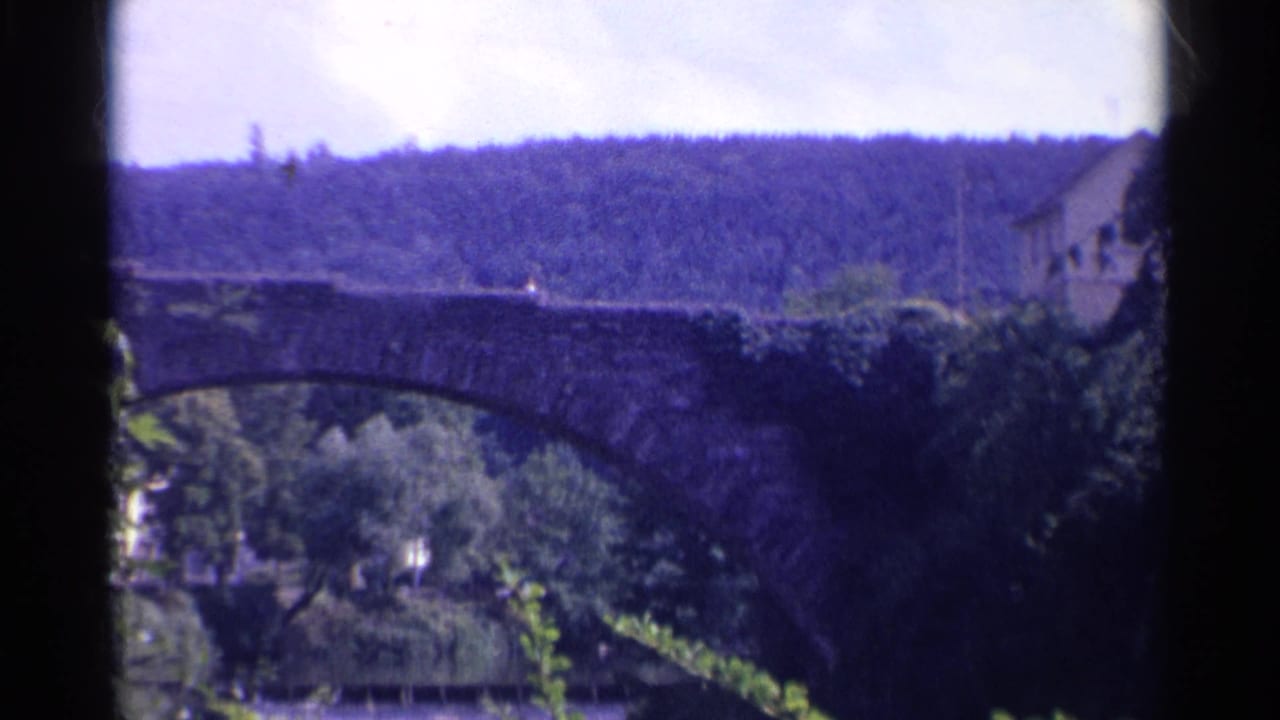 The final frame holds on the stone bridge, wooded riverbank, and distant hillside in soft 8mm color.