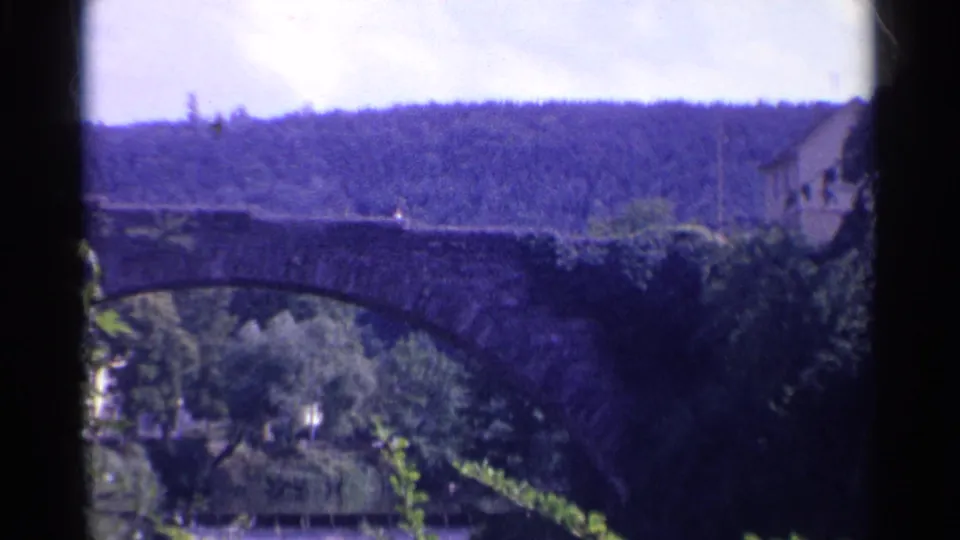 The final frame holds on the stone bridge, wooded riverbank, and distant hillside in soft 8mm color.