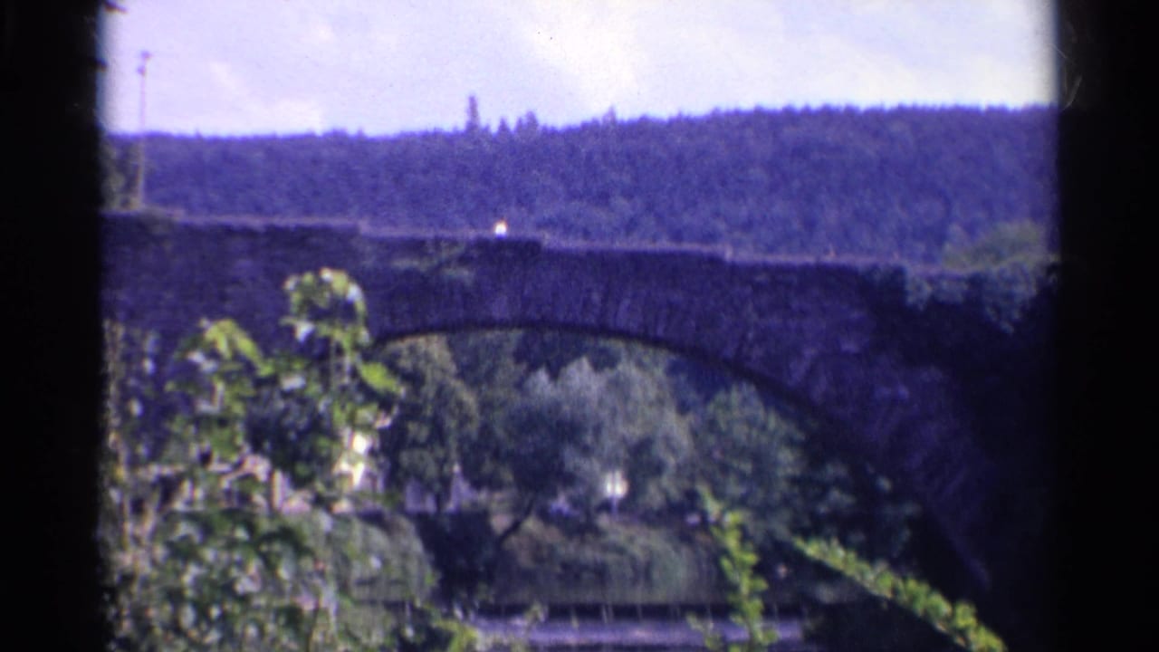 Stone arch bridge over a wooded river valley with hills beyond.