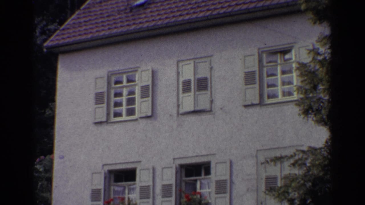 1961 Germany home-movie view of a pale stucco house with shuttered windows, flower boxes, and dark film border at the left edge.